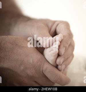 les mains poilues du père tiennent les orteils minuscules du bébé Banque D'Images