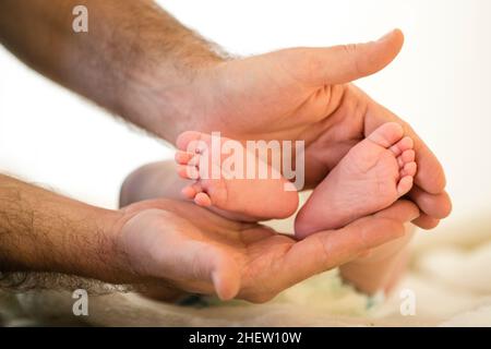 le père tient avec les mains les pieds du petit bébé avec les orteils crapanés Banque D'Images