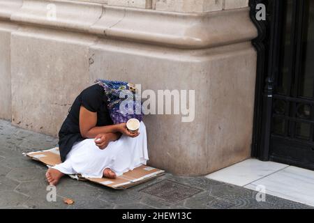 Une femelle napieds nus, pauvre, se lâcha sur un vieux morceau de carton, un renflement avec son visage caché et une tasse de mendicité dans sa ha Banque D'Images