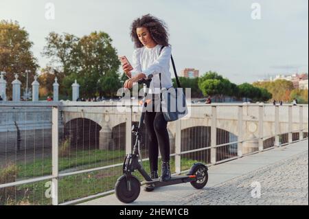 Une jeune femme télécharge l'application pour utiliser le scooter électrique en ville rue saine style de vie durable style de vie Banque D'Images