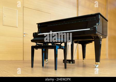 le paino de concert noir est debout sur une scène en bois avec tabouret prêt à jouer Banque D'Images