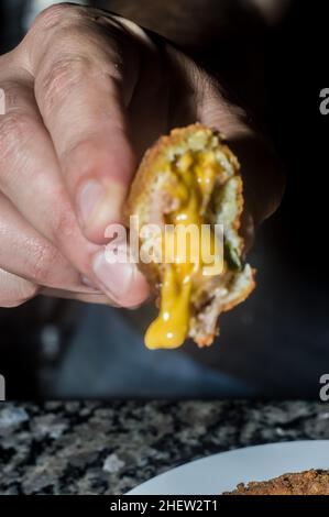 Boulettes de saucisse au fromage cheddar et sur une assiette en acier et tenue à la main, arrière-plan sombre et espace de copie, Banque D'Images