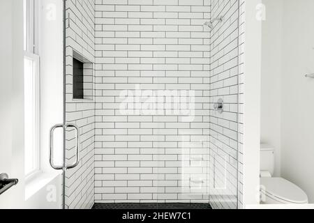 Coffret de douche moderne à carreaux de métro blanc avec plancher en carreaux hexagonaux noirs et porte en verre Banque D'Images
