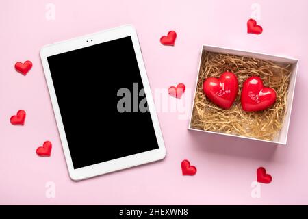 Tablette numérique pour choisir des cadeaux, faire l'achat, enveloppe, coeur rouge sur table rose vue du dessus plat Lay liste d'achats de vacances, bonne Saint-Valentin Banque D'Images