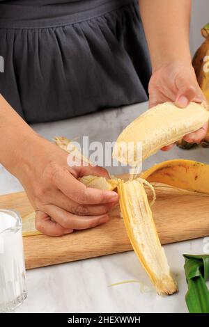 Femme épluchant à la main délicieux Banana sur une table en bois, préparer Kolak dans la cuisine Banque D'Images