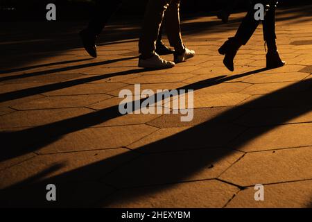 Silhouettes de jambes de personnes marchant dans la rue de la ville à l'heure du soir.De longues ombres au soleil doré du soir.Mise au point sélective. Banque D'Images