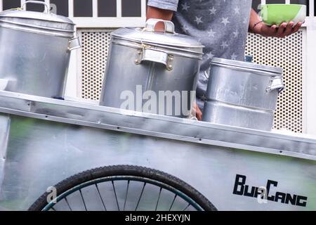 homme de rue vendeur de nourriture servant le porridge indonésien traditionnel de haricots verts sur son chariot d'argent Banque D'Images