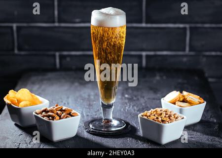 Verre de bière avec mousse et quatre en-cas différents Banque D'Images