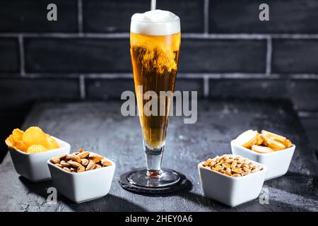 Verre de bière avec mousse et quatre en-cas différents Banque D'Images