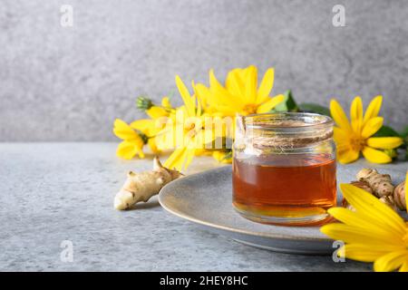 Sirop d'artichaut Jérusalem en bouteille, fleurs et racine sur fond gris. Copier l'espace. Banque D'Images