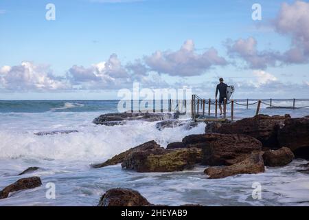 Le surfeur australien se dirige vers l'océan à Avalon Beach, tandis que de grandes vagues se déferlent dans la piscine de la plage, à Sydney en été, en Nouvelle-Galles du Sud, en Australie Banque D'Images