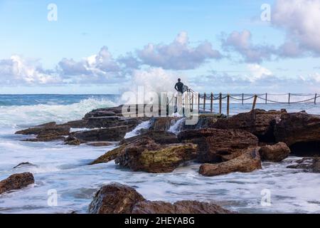 Le surfeur australien se dirige vers l'océan à Avalon Beach, tandis que de grandes vagues se déferlent dans la piscine de la plage, à Sydney en été, en Nouvelle-Galles du Sud, en Australie Banque D'Images