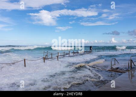 Le surfeur australien se dirige vers l'océan à Avalon Beach, tandis que de grandes vagues se déferlent dans la piscine de la plage, à Sydney en été, en Nouvelle-Galles du Sud, en Australie Banque D'Images