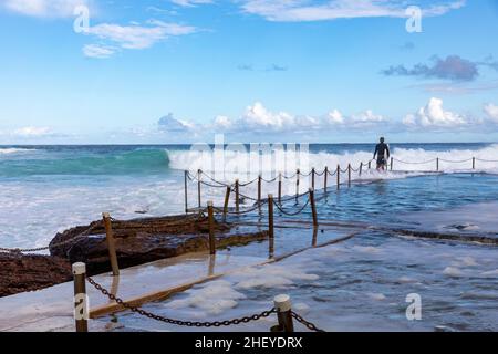 Le surfeur australien se dirige vers l'océan à Avalon Beach, tandis que de grandes vagues se déferlent dans la piscine de la plage, à Sydney en été, en Nouvelle-Galles du Sud, en Australie Banque D'Images