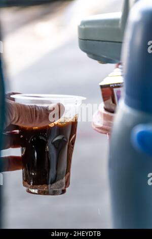 Le vendeur de nourriture de rue MAN verse une eau chaude de la verseuse pour faire un café noir sur la tasse en plastique transparent Banque D'Images