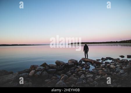 Lever de soleil givré bleu-rouge-rose au lac Oulujarvi près de la ville de Paltamo dans la région de Kainuu, en Finlande.Un explorateur en robe noire bénéficie de la vue de la c Banque D'Images