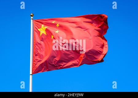 Le drapeau national de la République populaire de Chine vole dans le vent en mât complet contre le ciel bleu. Banque D'Images