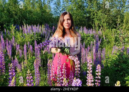 Portrait de la jeune femme caucasienne avec de longs cheveux rouges, sur fond de verdure dans le champ de lupin.Belle cueillette de fleurs femelle. Banque D'Images