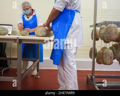 Travailleur spécialisé couture et finition des coupes à froid de culatello, de coppa et de prosciutto dans l'usine de fabrication de produits délicats de Parme en Italie Banque D'Images