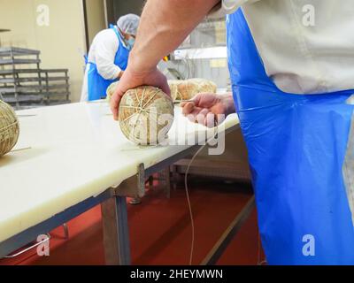 Travailleur spécialisé couture et finition des coupes à froid de culatello, de coppa et de prosciutto dans l'usine de fabrication de produits délicats de Parme en Italie Banque D'Images