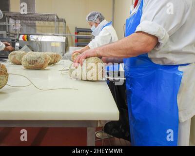 Travailleur spécialisé couture et finition des coupes à froid de culatello, de coppa et de prosciutto dans l'usine de fabrication de produits délicats de Parme en Italie Banque D'Images