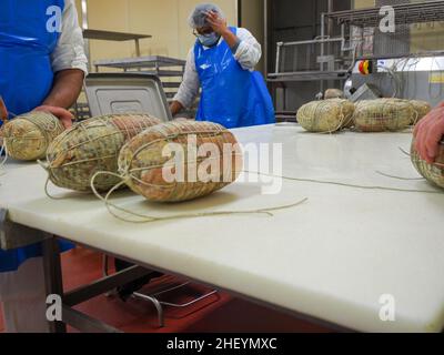 Travailleur spécialisé couture et finition des coupes à froid de culatello, de coppa et de prosciutto dans l'usine de fabrication de produits délicats de Parme en Italie Banque D'Images