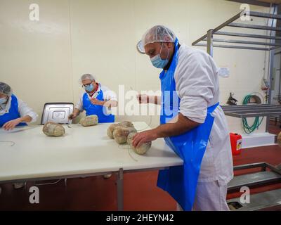 Travailleur spécialisé couture et finition des coupes à froid de culatello, de coppa et de prosciutto dans l'usine de fabrication de produits délicats de Parme en Italie Banque D'Images