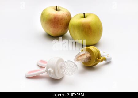 Grignoteuse avec pommes fraîches sur table blanche, gros plan.Alimentation bébé. Banque D'Images