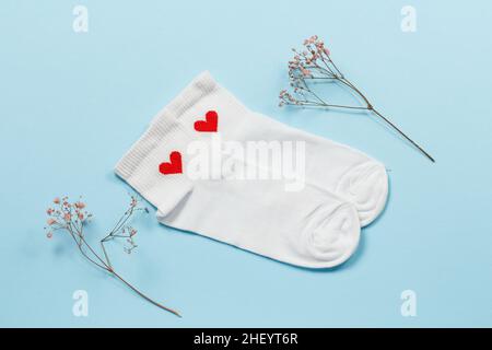 Paire de chaussettes blanches pour femmes et branches décoratives sur fond bleu, vue du dessus. Banque D'Images
