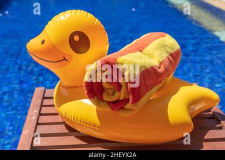 Canard gonflable jaune avec une serviette rayée roulée sur le côté de la piscine.Vacances, vacances d'été. Banque D'Images