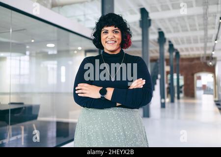 Femme d'affaires réussie debout avec ses bras croisés.Bonne femme d'affaires de taille moyenne qui regarde la caméra dans un lieu de travail moderne.FEM Banque D'Images
