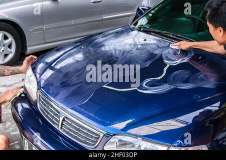 deux hommes frottent et polissent le capot de voiture bleu ou le capot moteur avec la main pour obtenir propre , brillant et brillant au garage pour les travaux de peinture et de détail automobile Banque D'Images