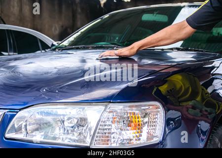 Homme frotter et polir le capot de voiture bleu ou le capot moteur avec la main pour obtenir propre , brillant et brillant au garage pour les travaux de peinture et de détail de la compa automobile Banque D'Images