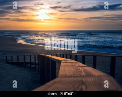 Paysage de coucher de soleil doré sur la plage montrant un gros plan flou de la main courante en bois de la promenade menant au sable et à l'océan Atlantique Banque D'Images