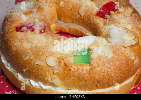 Grand gâteau de beignet garni de crème fouettée sucrée avec des fruits confits ornant le dessus sur une nappe décorée avec des motifs de Noël.swe traditionnelle Banque D'Images