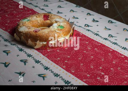 Un grand gâteau en forme de beignet rempli de crème fouettée et décoré de fruits confits rouges et verts sur une nappe décorative de Noël.Roscon de Rey Banque D'Images