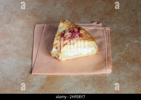 Portion d'une génoise crémeuse décorée d'amandes confites et de baies rouges enrobées de sucre glace sur une élégante serviette. Banque D'Images