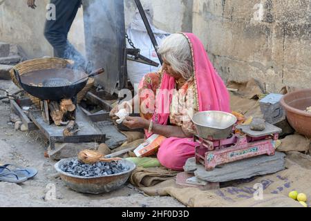 Une femme indienne âgée de la région portant un rose sari cuisine la nourriture de rue sur un feu de charbon de bois dans le village de Nagda, près d'Udaipur, Rajasthan, Inde Banque D'Images