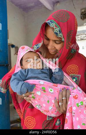 Une jeune mère indienne locale portant un sari rose berce son bébé dans sa maison dans le village de Nagda, près d'Udaipur, Rajasthan, Inde, Asie du Sud Banque D'Images