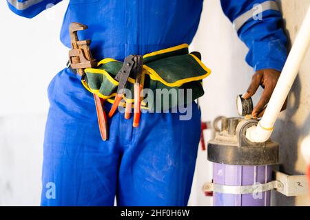 Gros plan d'un plombier ou d'un réparateur non reconnaissables inspectant en vérifiant la machine à filtre à eau sur le chantier de construction - concept de collier bleu Banque D'Images