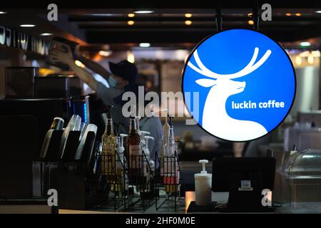 Fermez l'affiche de la marque Luckin Coffee en magasin.Marque de café chinoise.Personnel dans le masque facial Banque D'Images