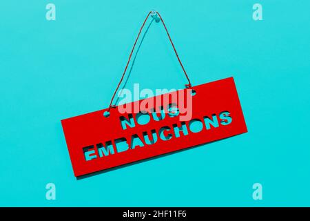 le texte que nous embauchons, écrit en français, est découpé sur un panneau rouge, suspendu sur fond bleu Banque D'Images