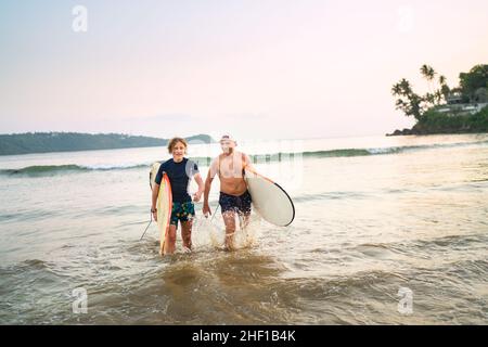 Portrait d'un jeune garçon avec son père avec des planches de surf après le surf.Ils sourient et sortent de l'eau.Vacances actives en famille ou actives Banque D'Images