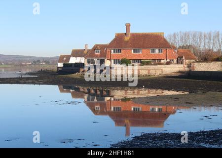 Bâtiment résidentiel adjacent à Bosham Meadow Green avec réflexion du bâtiment dans l'eau.Le parc national de South Downs se trouve au loin. Banque D'Images