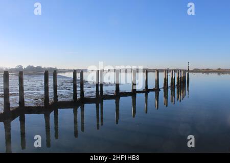 Les postes d'amarrage à Bosham Quay se reflètent dans les eaux fixes.Espace de copie bleu clair pour ajouter du texte. Banque D'Images