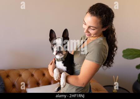 Femme caucasienne souriant tout en tenant son chien de chiot à la maison Banque D'Images