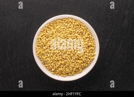 Le millet biologique non cuit groats dans une soucoupe blanche sur une pierre d'ardoise, macro, vue de dessus. Banque D'Images