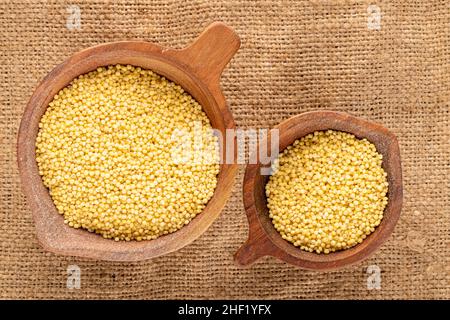 Gruaux de millet biologique brut dans deux tasses en bois sur le burlap, macro, vue de dessus. Banque D'Images