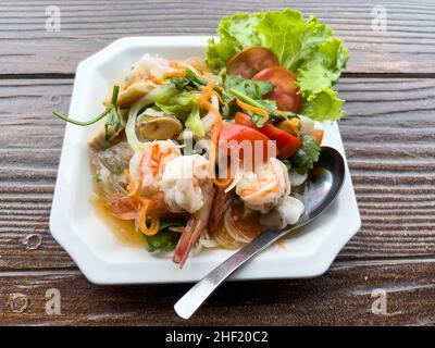 Gros plan de la salade de fruits de mer thaï épicée servie dans la plaque blanche pour un apéritif dans le restaurant thaïlandais, au-dessus de la vue avec l'espace copie. Banque D'Images