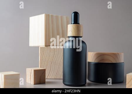 Bouteille de maquillage noire et pot de crème sur fond de cubes en bois.Marque de produits de beauté à base de plantes, design d'emballage de produits de beauté naturels. Banque D'Images